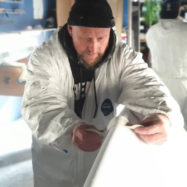 Using abrasives to sand the rail of a surfboard at The Surfboard Studio