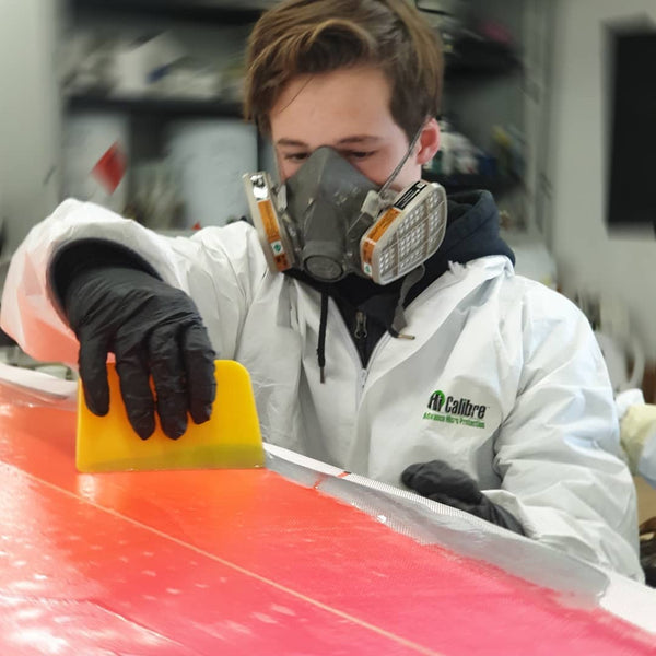 Glassing a surfboard with a squeegee at The Surfboard Studio