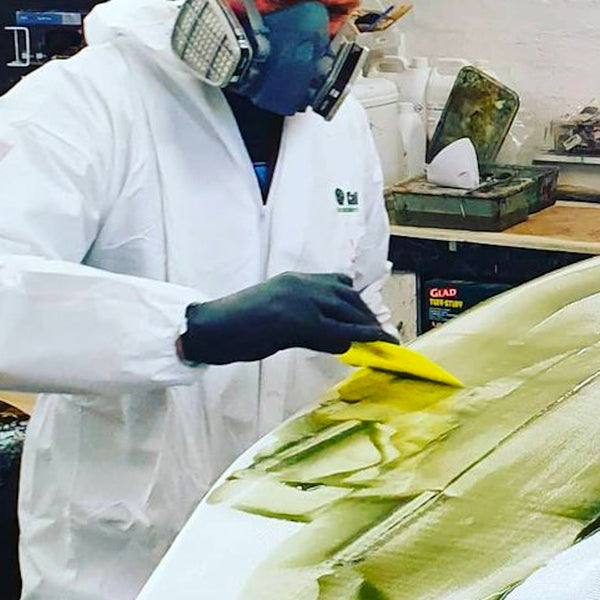 Glassing a surfboard with protective gloves.