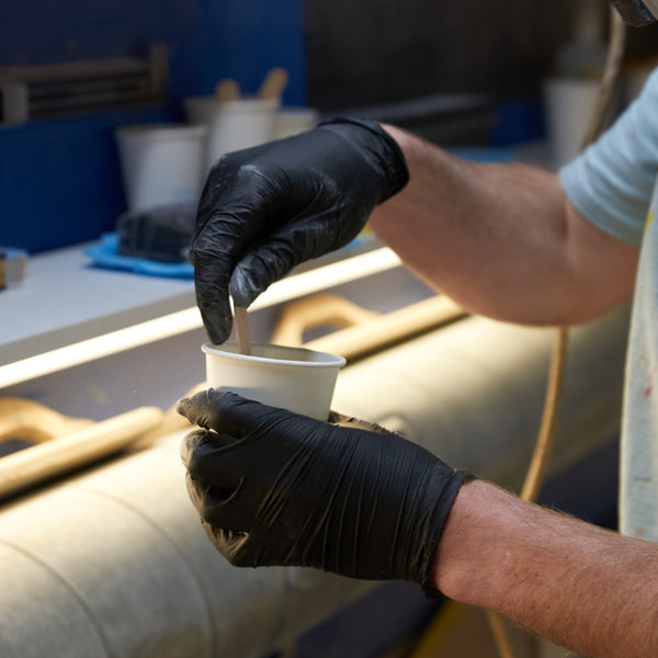 Using a tongue depresser and cup to mix resin for a surfboard repair